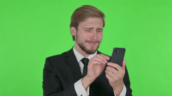 Young Businessman Loss on Smartphone on Green Background
