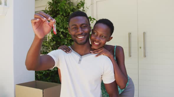 Portrait of smiling african american couple holding house keys and embracing outside their home
