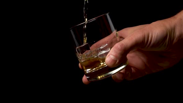 Pouring golden whiskey into a glass with ice cubes