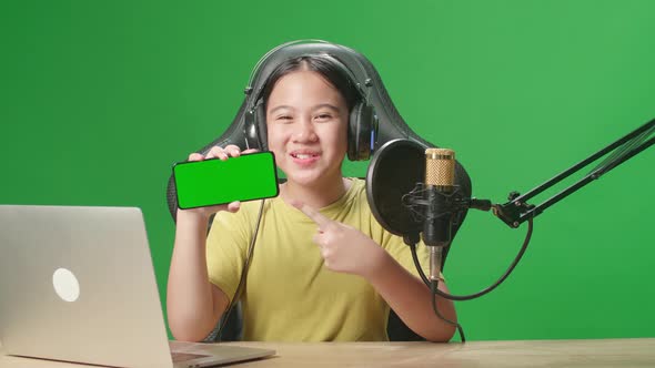 Asian Kid Girl Holding Phone With Mock Up Green Screen While Live Stream In Green Screen Studio