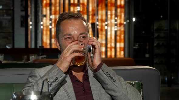 Cheerful Businessman Drinking Whiskey While Talking on the Phone