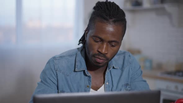 Portrait of Concentrated African American Young Man Working Online Messaging on Laptop