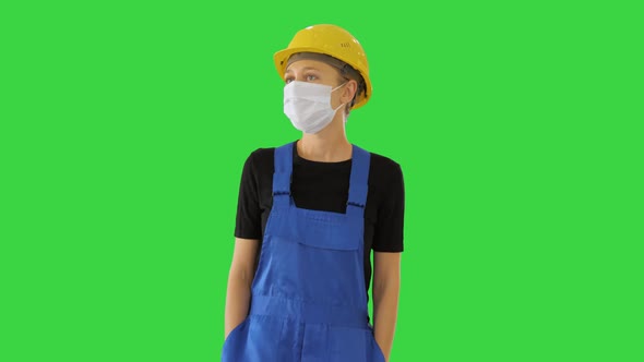 Young Woman in Yellow Hardhat and in Medical Mask Walking on a Green Screen, Chroma Key.