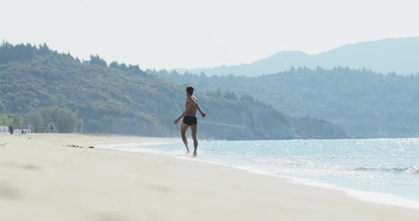 The Handsome Man with a Perfect Athletic Body in Swimming Trunks Having Fun on a Deserted Beach in