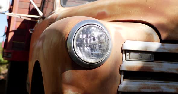 Close up shot of the front of an old rusty vintage truck fender with glass headlight and grill in th