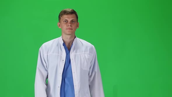 Medical Man in White Coat Going and Looking Forward Against a Green Background. Slow Motion.