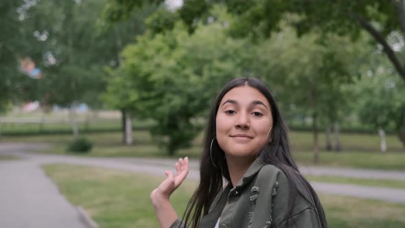 A Young Brunette Girl in a Good Mood in White Sneakers Whirls and Dances in the Park To the Music