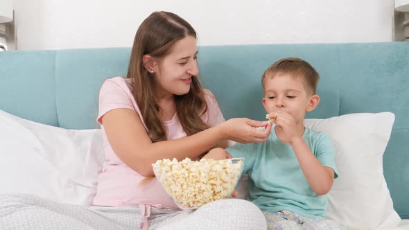 Little Toddler Boy with Young Mother in Pajamas Lying in Bed on Weekend and Eating Popcorn From Big