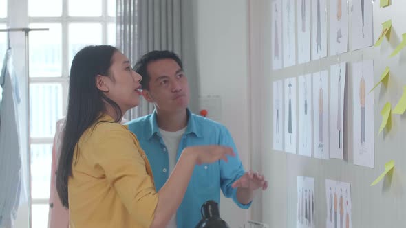 Asian Male And Female Designers Helping Each Other Putting The Picture On The Wall Before Discussing