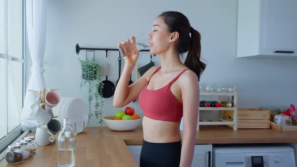 Asian beautiful woman in sportswear drink water after workout for health care in kitchen in house.