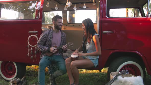 Happy Young Mixed Race Couple Playing Instruments and Having Some Fun in Retro Hippie Minibus in