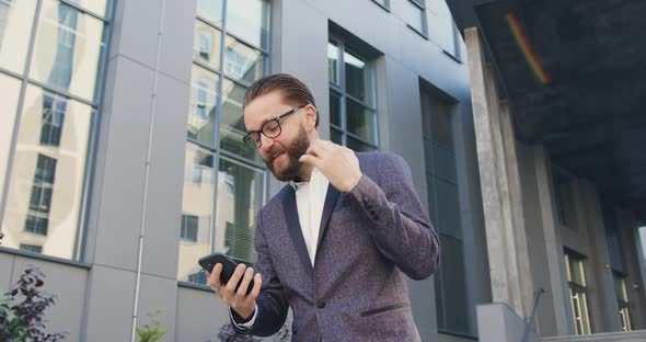 Office Worker in Glasses which is Surprised from Good News on Phone Screen while Standing