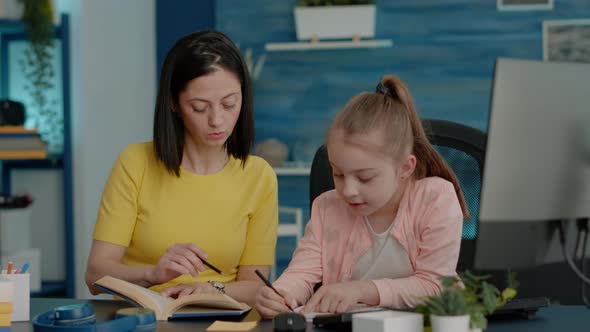 Schoolgirl Writing on Notebook and Checking Book for Information