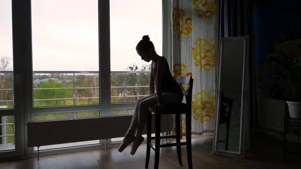 Dark Silhouette of Little Ballet Dancer, Girl in a Ballet Leotard, Resting Sitting on Chair After