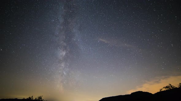 Timelapse of the Milky Way in summer in Germany. In the foreground is forest. Over time clouds pass