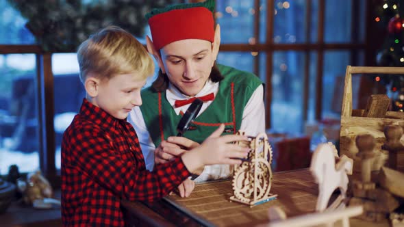 An Elf with Long Ears is Holding a Magnifying Glass in His Hand and Showing a Little Boy a Funny Toy