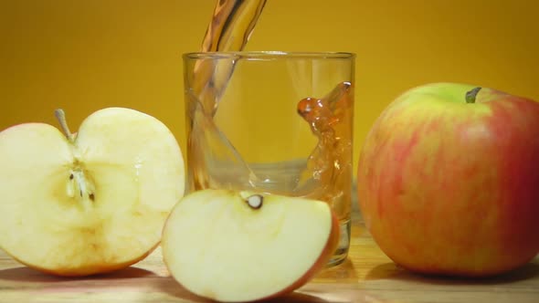 Apple Juice is Poured in a Glass Next to Apple Slices on the Yellow Background