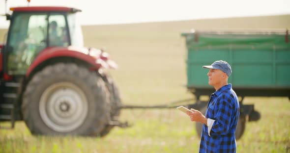 Farmer Using Digital Tablet While Looking at Tractor in Farm