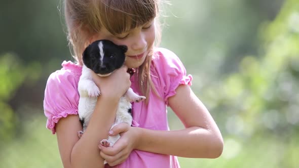 Pretty child girl playing with little puppy outdoors in summer.