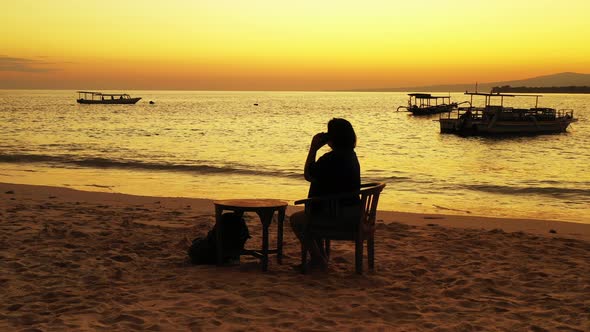 Silhouette of girl talking on smartphone, sitting on exotic beach, watching beautiful sunset with ye