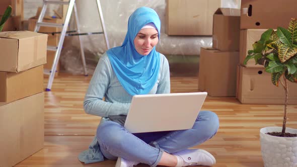 Portrait Young Muslim Woman in a Hijab Uses a Laptop Sitting on the Floor Next To the Boxes