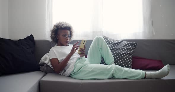 Latin American Woman on the Sofa at Home Chatting with a Smartphone