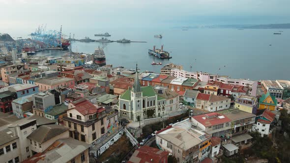 Aerial dolly in of colorful houses and Lutheran Church leading to Valparaiso Sea Port and ships dock