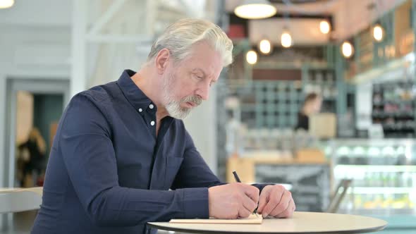 Thoughtful Old Man Doing Paperwork in Cafe