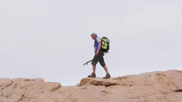 Senior hiker man with backpack and trekking poles walking on the rocks