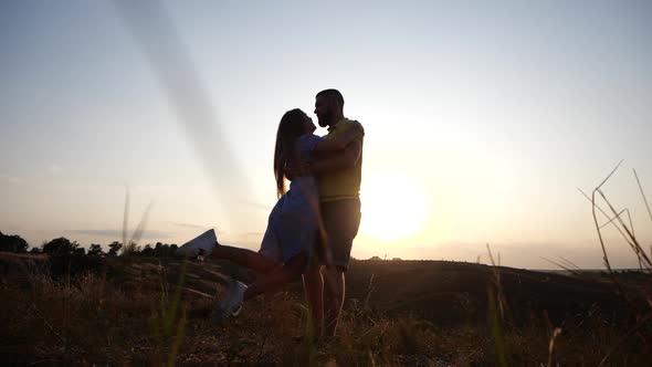 A Love Story of a Young Charming Couple in Rural Landscape at Sunset. Silhouette of Bearded Young