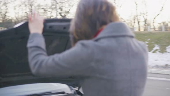 Attractive Business Woman in Grey Coat Opening the Car's Bonnet and Looking Under the Hood in the