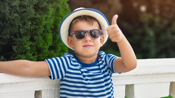 Cute Little Boy in Hat and Sunglasses Showing Cool Gesture Thumb Up Having Good Time Outdoor