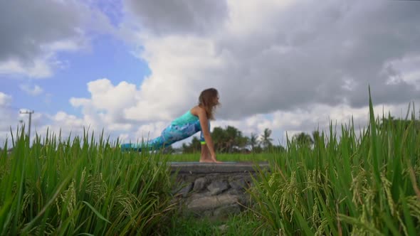 Slowmotion Steadicam Shot of a Young Woman with Yoga Math Walking Through a Beautiful Rice Field