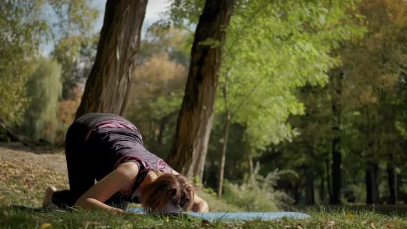 Woman Sitting on Yoga Mat and Practicing Yoga Stretching Exercise Outdoors in Sunny Day