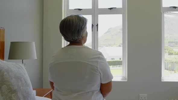 Rear view of senior black woman sitting on bed in bedroom of comfortable home 4k