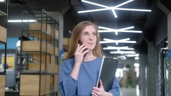 businesswoman with smartphone and documents walks down corridor of office