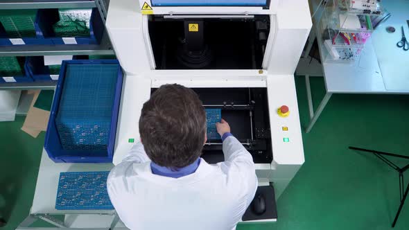 the Worker Puts the Motherboard Into the Electrical Board Inspection Equipment. Printed Circuit