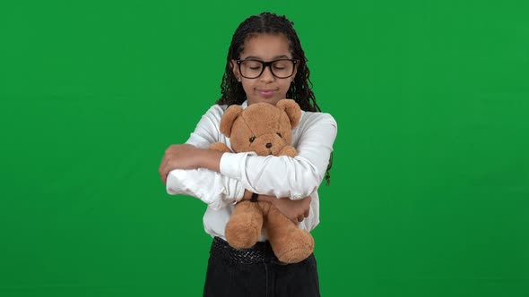 Portrait of Cute Unhappy African American Teen Girl Hugging Teddy Bear Standing on Green Screen
