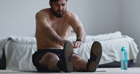 Young Man Stretching His Body, Sitting on Floor at Home