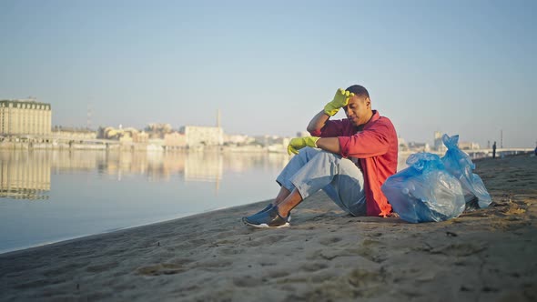 Man Sitting on Beach Looks at Clean Sand with Satisfaction