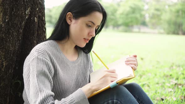 Young Attractive Woman Writing Something on Notebook and Smiling in the Public Park