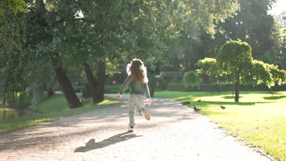 Back View Cheerful Little Girl Running in Sunshine in Spring Summer Park in Slow Motion