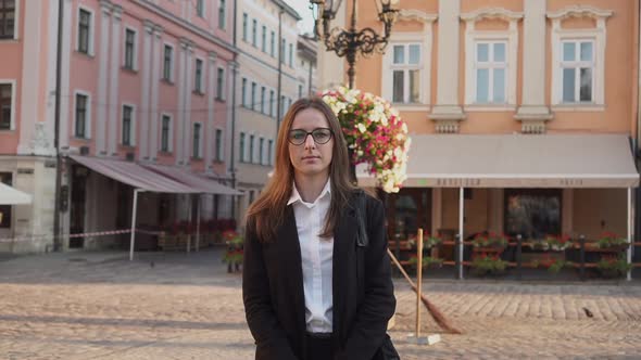 Portrait of Young Successful Businesswoman with Glasses Standing in the Street Looking at Camera