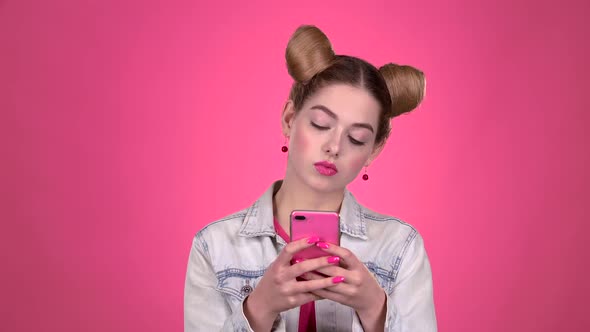 Teen in a Pink Topic Prints a Message on the Phone. Pink Background. Slow Motion