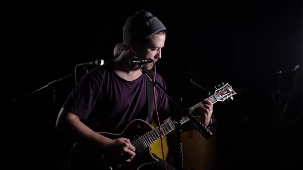 A Man Plays an Electric Guitar and Sings in a Dark Room