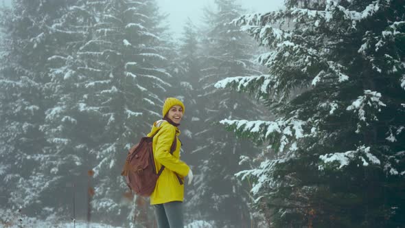 Happy Joyful Woman in Yellow Warm Clothing Invites to Follow Her at Winter Forest with Falling Snow