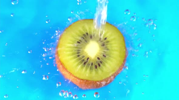 Water pours on green hue juicy kiwi fruit on cyan background slow motion closeup. Kiwi fruit slice