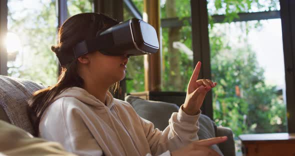 Asian girl smiling and gesturing while wearing vr headset sitting on the couch at home