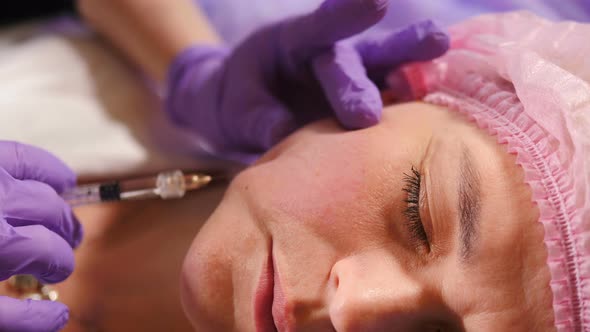 Beautician Making Facial Filler Injection Into Female Cheekbone