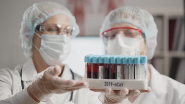 Scientists in Protection Clothing Holding Tray with Covid-19 Positive Blood Samples in Laboratory